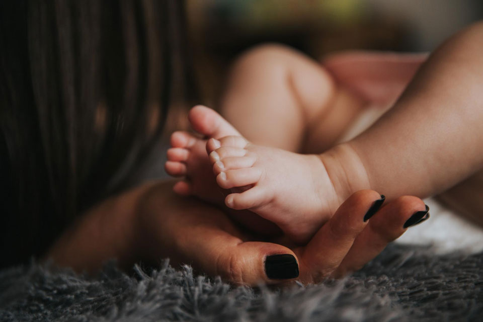 A close up of Hands holding baby feet on a gray carpet.